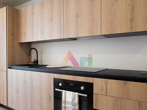 A modern kitchen with wooden cabinets, a black countertop, a built-in oven, and a digital clock. - Elegant Garden Suite in Anse Marcel (Saint-Martin)