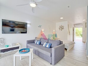 Ein modernes Wohnzimmer mit einem grauen Sofa, einem kleinen weißen Tisch und einem Deckenventilator.