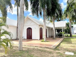 A white building with a covered porch, palm trees, and a clear sky. - Studio in Anse Marcel (Saint-Martin)