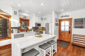 A modern kitchen with white cabinetry, a large island with bar stools, stainless steel appliances, and a wooden door. - Ski in/out to Tamarack Express Chairlift, pet-friendly, AC, hot tub (Tamarack)