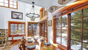 A dining area with a wooden table set for four, surrounded by large windows offering a view of a snowy landscape. - Ski in/out to Tamarack Express Chairlift, pet-friendly, AC, hot tub (Tamarack)