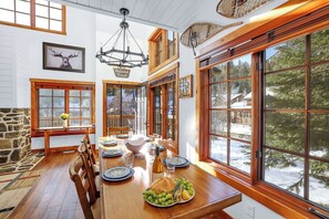 A dining area with a wooden table set for four, surrounded by large windows offering a view of a snowy landscape. - Ski in/out to Tamarack Express Chairlift, pet-friendly, AC, hot tub (Tamarack)