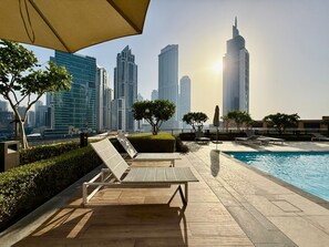 Un área de piscina en la azotea con sillones de descanso, una piscina y un horizonte urbano de fondo.