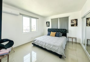A bedroom with a bed, a chair, a small table, and artwork on the walls. - ORION APARTMENT (Hatillo)
