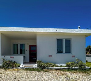 A single-story building with a white exterior, a red door, and two windows. There are signs indicating reserved parking. - ORION APARTMENT (Hatillo)