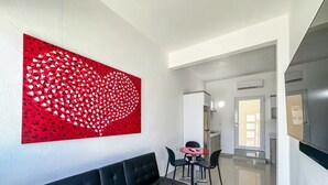 Ett modernt vardagsrum med en svart soffa, ett rött, abstrakt konstverk och ett matbord med stolar.