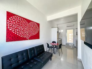 A modern living area with a black sofa, a red abstract art piece, and a dining table with chairs. - CASSIOPEIA APARTMENT (Hatillo)