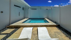 En swimmingpool med två solstolar, omgiven av ett vitt staket och en klarblå himmel.