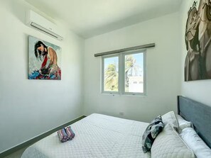 A bedroom with a bed, a window, and a painting on the wall. - CASSIOPEIA APARTMENT (Hatillo)