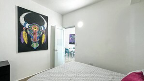 Quarto com cama, porta para área de refeições e obra de arte na parede.