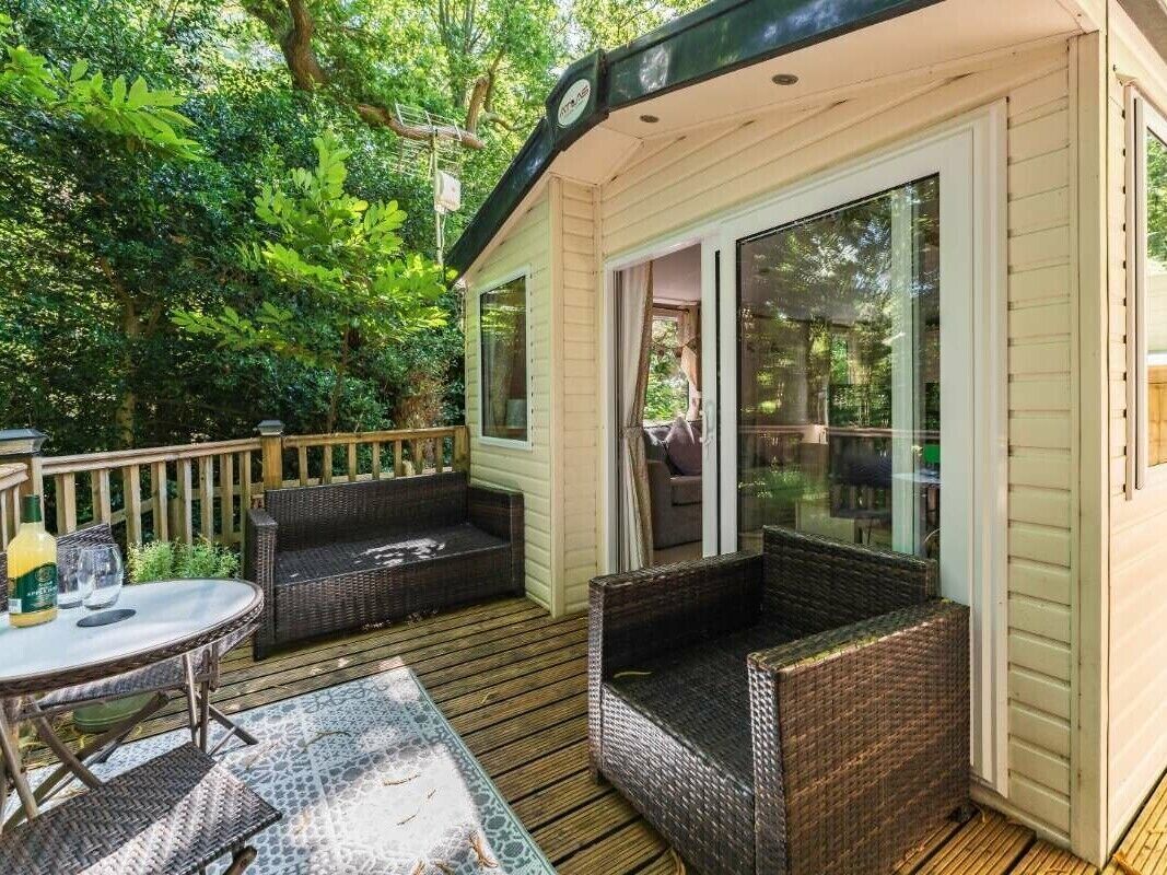 A covered outdoor seating area with wicker furniture, a glass table, and a wooden deck.