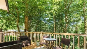 A wooden deck with wicker furniture and a small table, surrounded by lush greenery. - Two Hoots - Kelling Heath Holiday Park - 19668 (Holt)