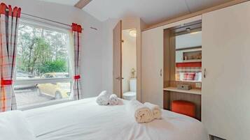 A hotel room with a bed, a window with curtains, a bathroom, and a wardrobe.