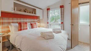 A bedroom with a bed, bedside tables, a wardrobe, a window with curtains, and a door. - Two Hoots - Kelling Heath Holiday Park - 19668 (Holt)