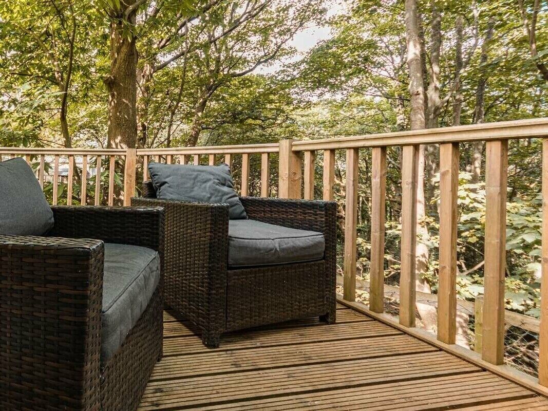 Una terraza de madera con mobiliario de mimbre y barandilla.