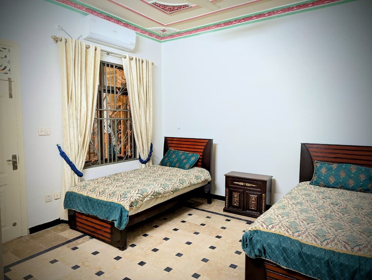 Una habitación con dos camas, un armario pequeño y una ventana con cortinas.