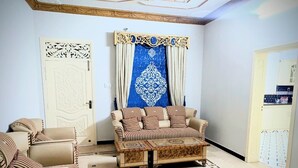 Une pièce avec un canapé beige, un fauteuil assorti et une table basse à motifs. Un rideau bleu décoratif est accroché au fond.