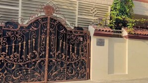 Une porte en fer forgé ornée de motifs complexes, un mur de briques et un toit recouvert de tuiles.