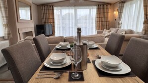Un comedor con una mesa de madera dispuesta para dos personas, una botella de champán y un televisor al fondo.