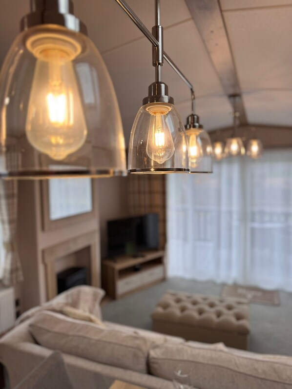 A modern living room with a sofa, a television, and pendant lights with exposed bulbs.