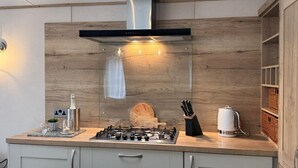 Una cocina moderna con estufa a gas, campana extractora de acero inoxidable, paneles de madera en la pared y un mueble empotrado con cesto.