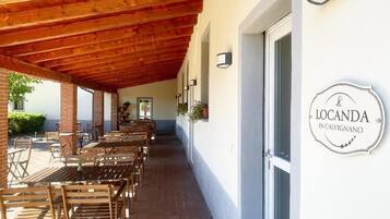 An outdoor patio with wooden tables and chairs, a covered area with a wooden ceiling, and a sign reading "Locanda in Calvignano".