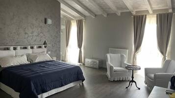 Un dormitorio con una cama grande, una silla blanca, una mesita pequeña y un radiador.