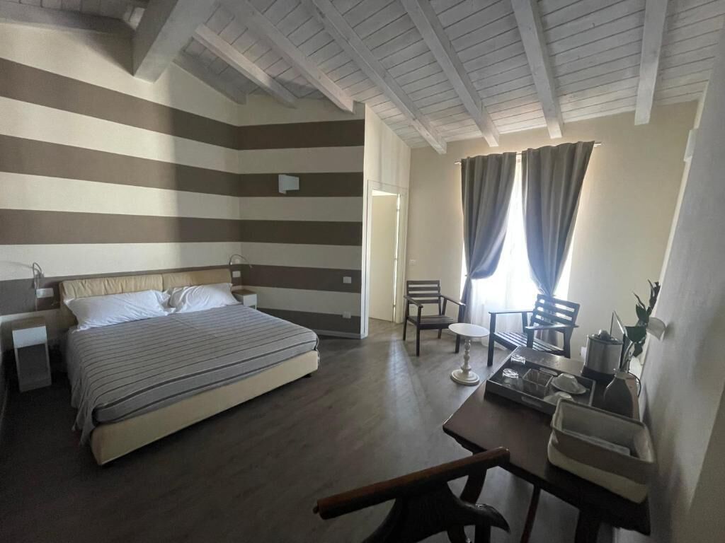 Un dormitorio con cama, escritorio y silla. Hay una ventana con cortinas y una puerta.