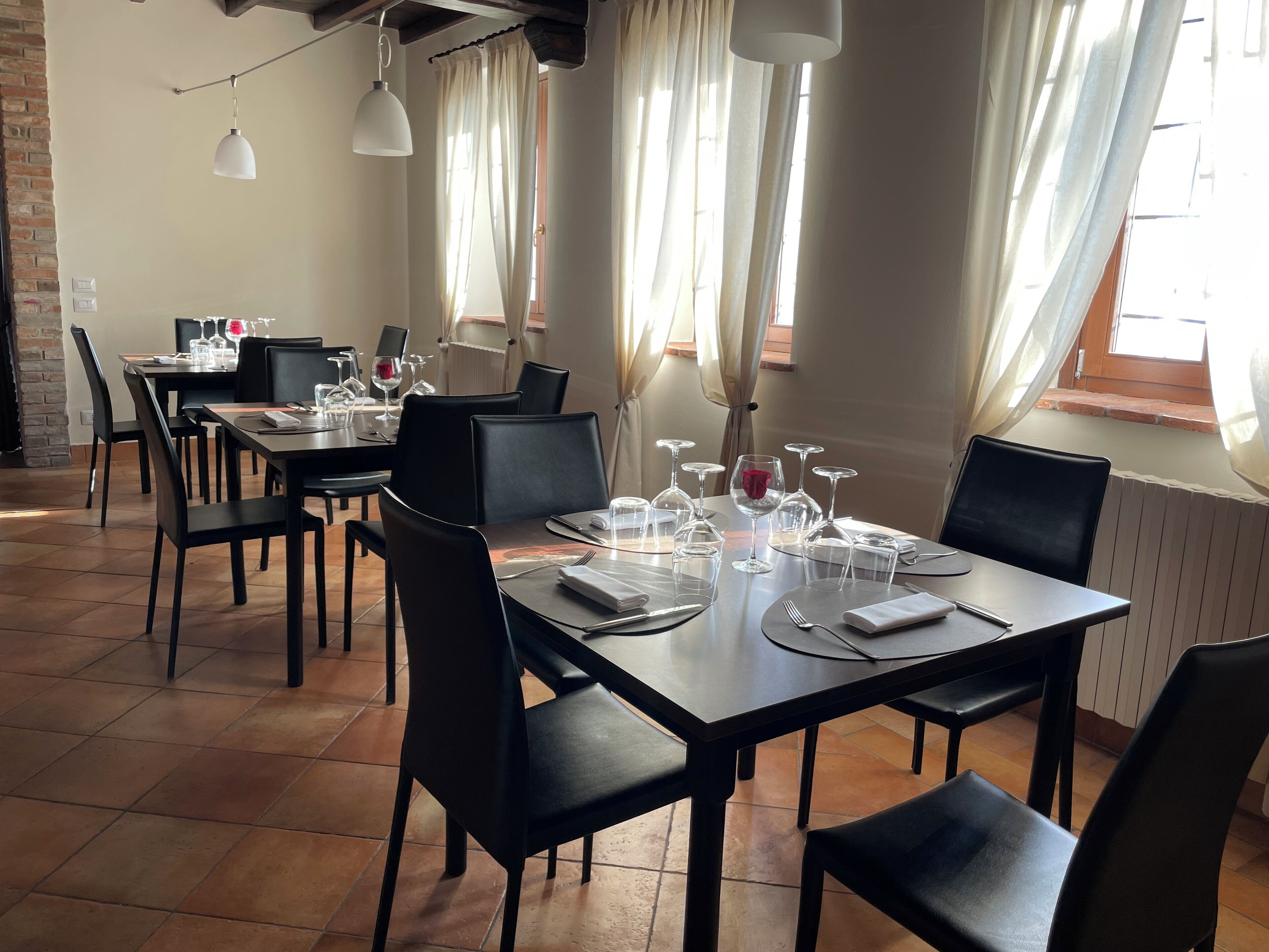 Un espace repas avec des tables préparées pour deux personnes, des chaises et un mur en briques.