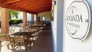 En utomhusplats med ett trädäck, träbord och stolar, ett tegelgolv och en skylt med texten "LOGANDA IN CALVIGNANO".