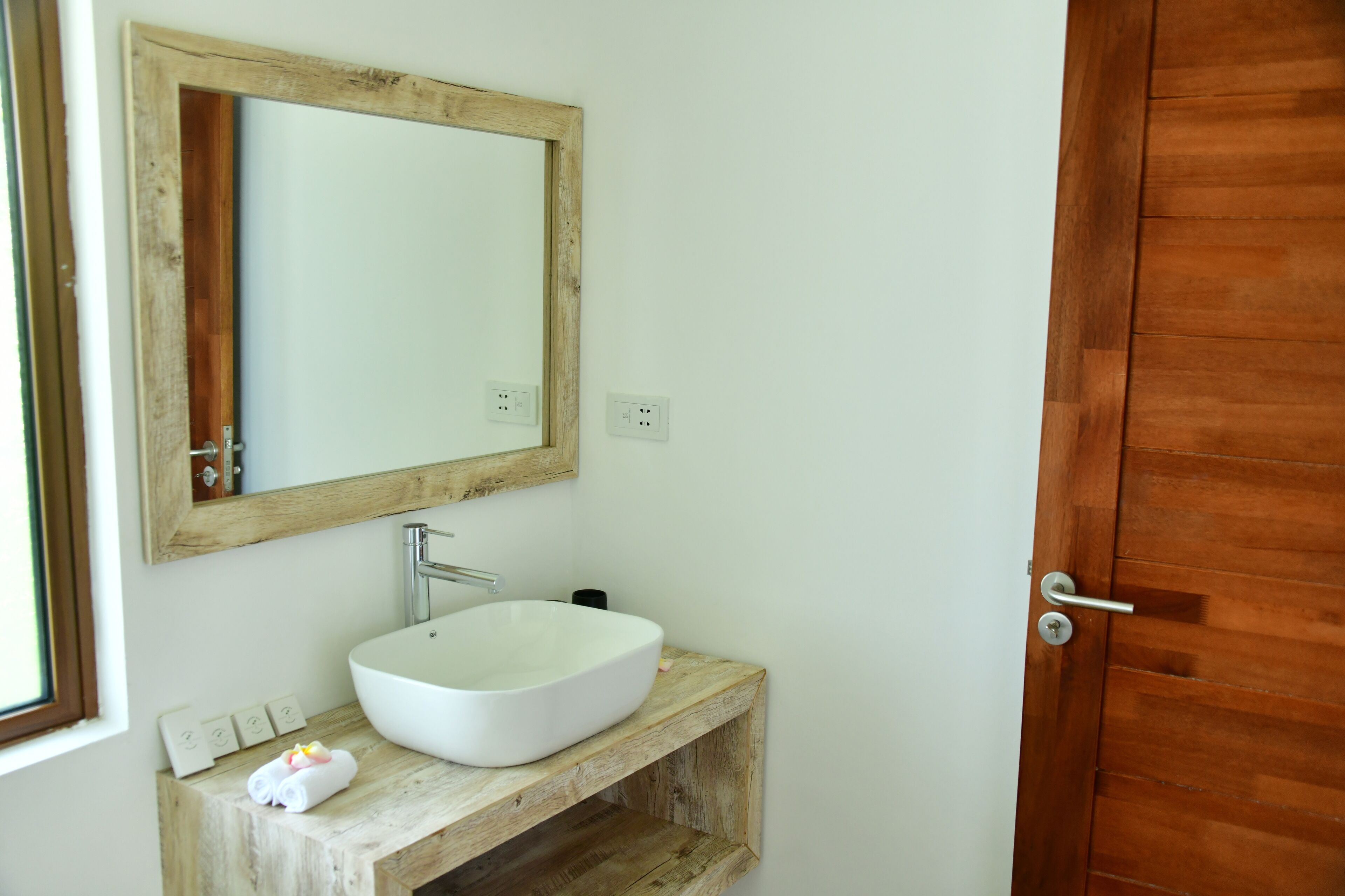 A bathroom with a wooden vanity, a white sink, and a mirror.