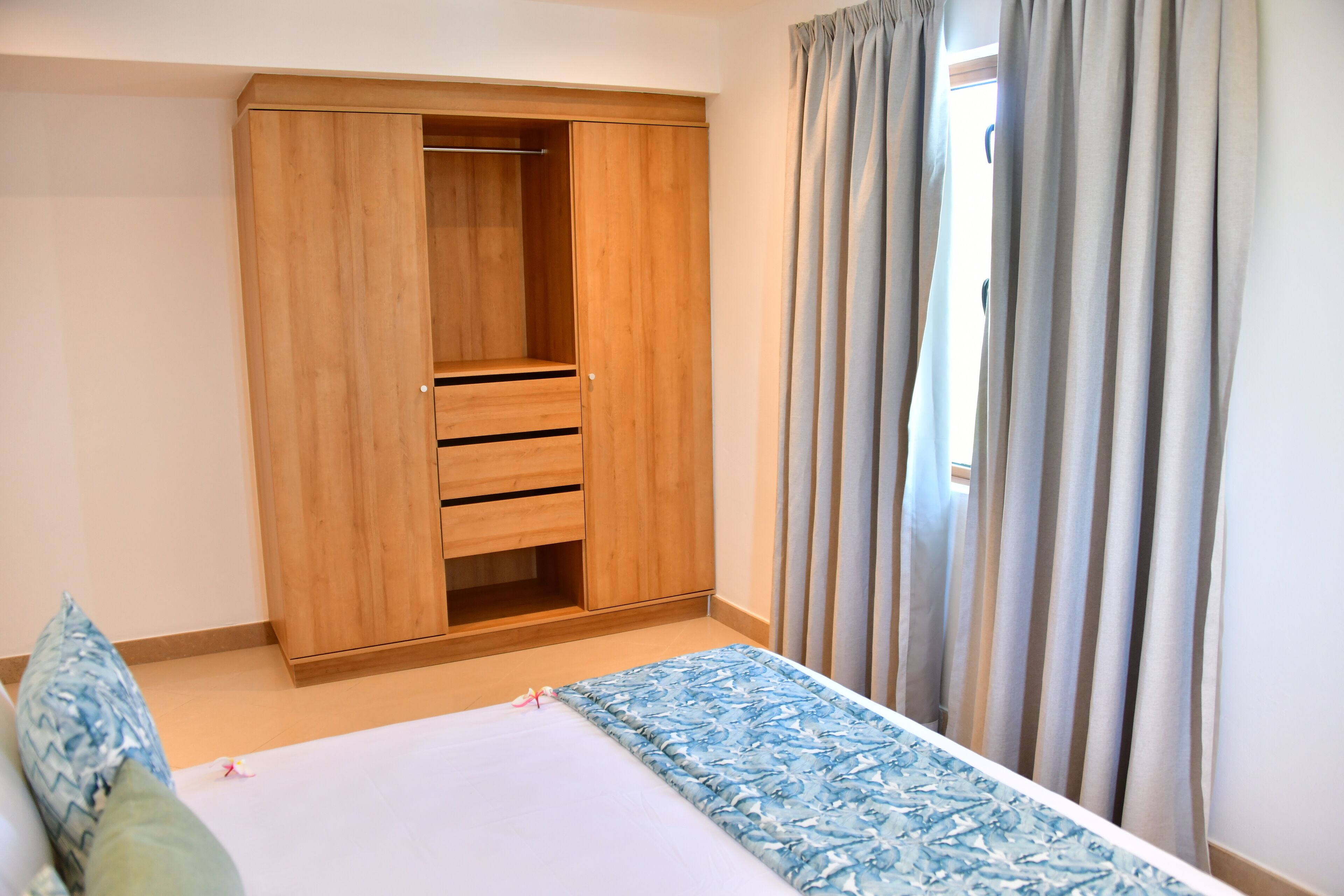 A bedroom with a wooden wardrobe, a bed with a patterned bedspread, and a window with curtains.