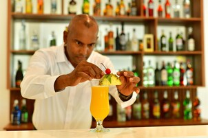Un cantinero preparando una bebida con una rodaja de piña y una cereza en un vaso.