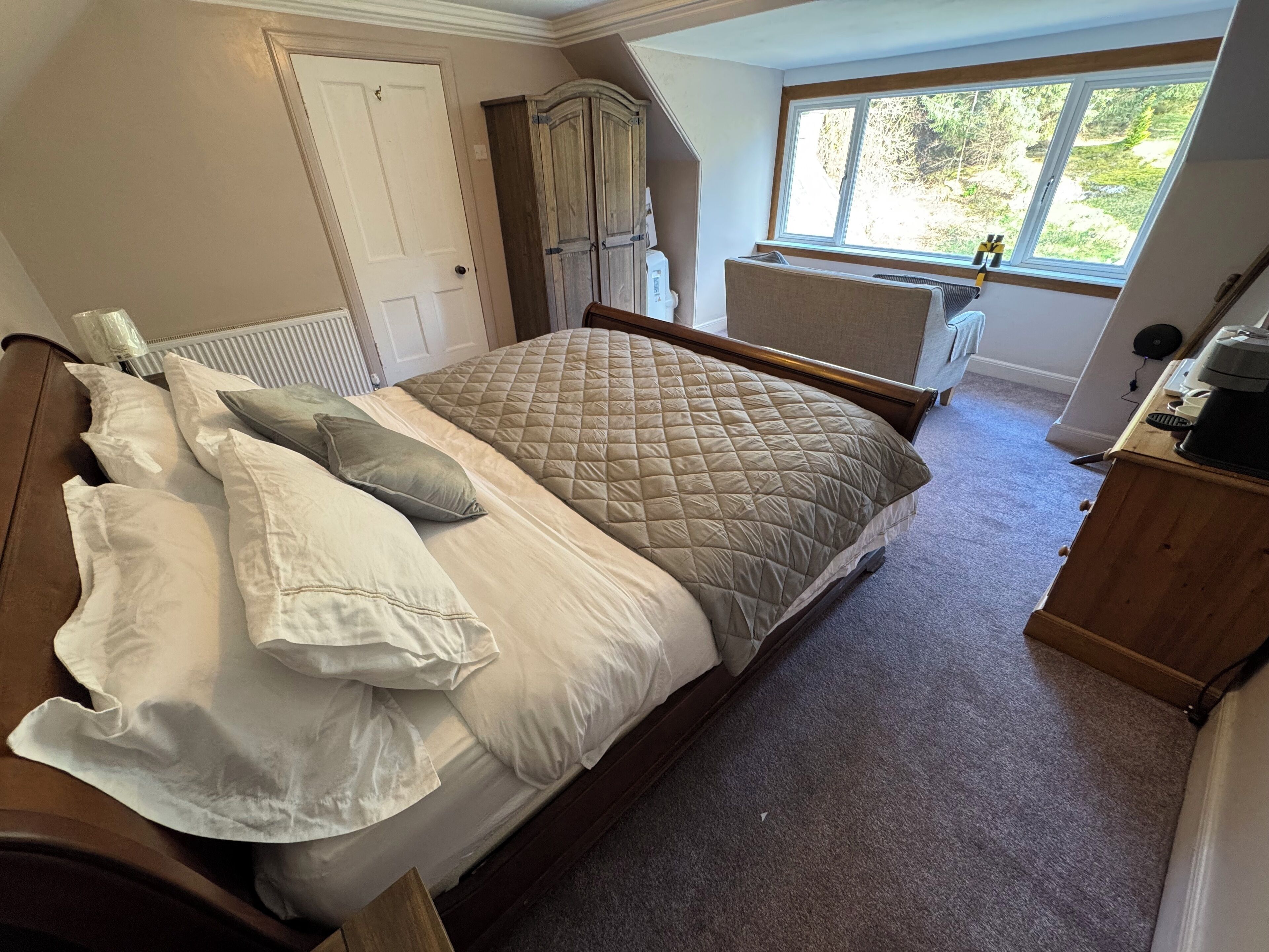 A bedroom with a large bed, a radiator, a window with a view, and a wooden wardrobe.