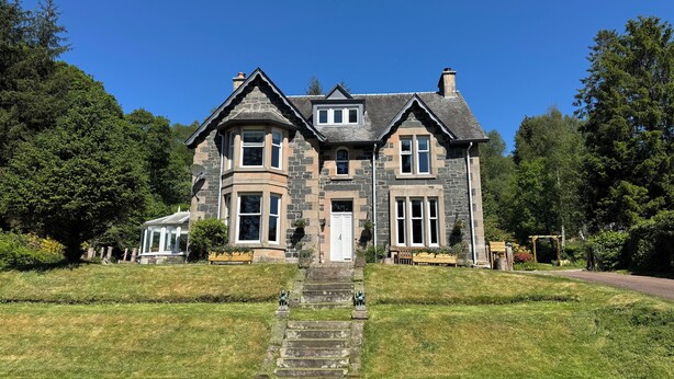 A large stone house with a prominent entrance, multiple windows, and a well-maintained lawn. - Crannaig House (Stirling)