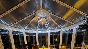 A covered dining area with tables and chairs, large windows, and string lights. - Crannaig House (Stirling)
