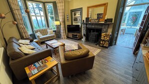 A cozy living room with a fireplace, a sofa, a coffee table, and a television. - Crannaig House (Stirling)