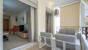 En moderne lejlighed med balkon, sofa, stol og fjernsyn.