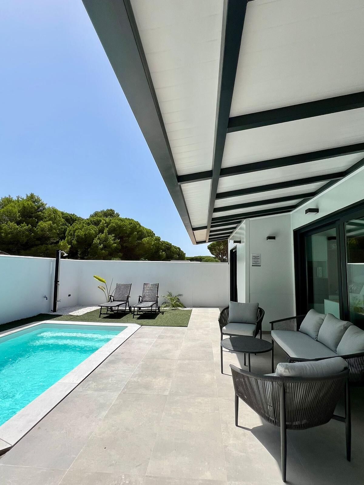 A modern outdoor patio with a swimming pool, lounge chairs, and a covered seating area.