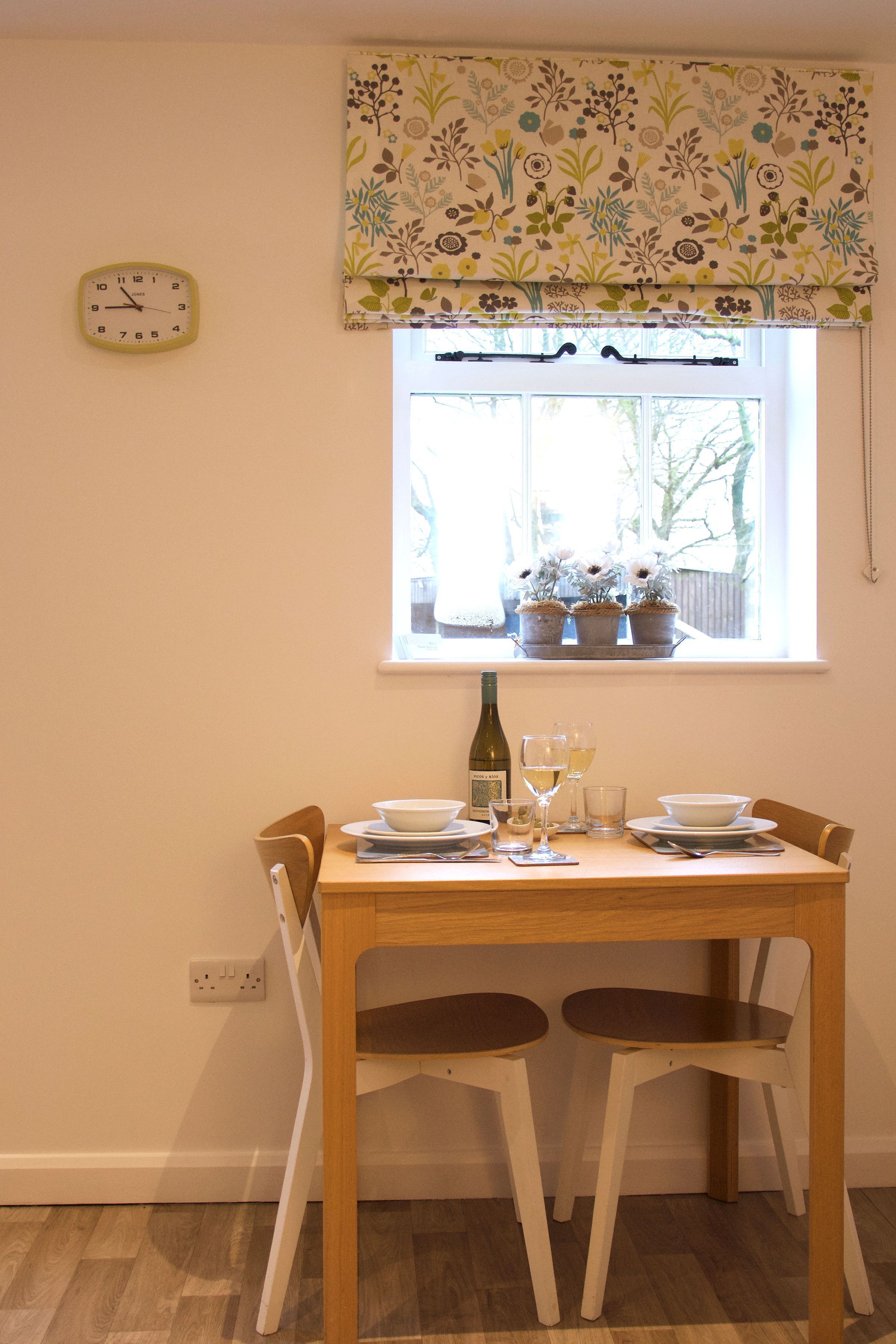 Une table à manger avec des chaises, une horloge et une fenêtre agrémentée de plantes en pot.