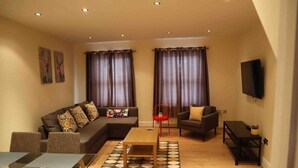 Ein Wohnzimmer mit einer Couch, Sesseln, einem Couchtisch, einem Fernseher und einem Essbereich mit Tisch und Stühlen.
