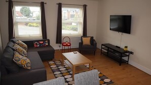 Ein modernes Wohnzimmer mit einer Couch, Sesseln, einem Couchtisch und einem Fernseher.