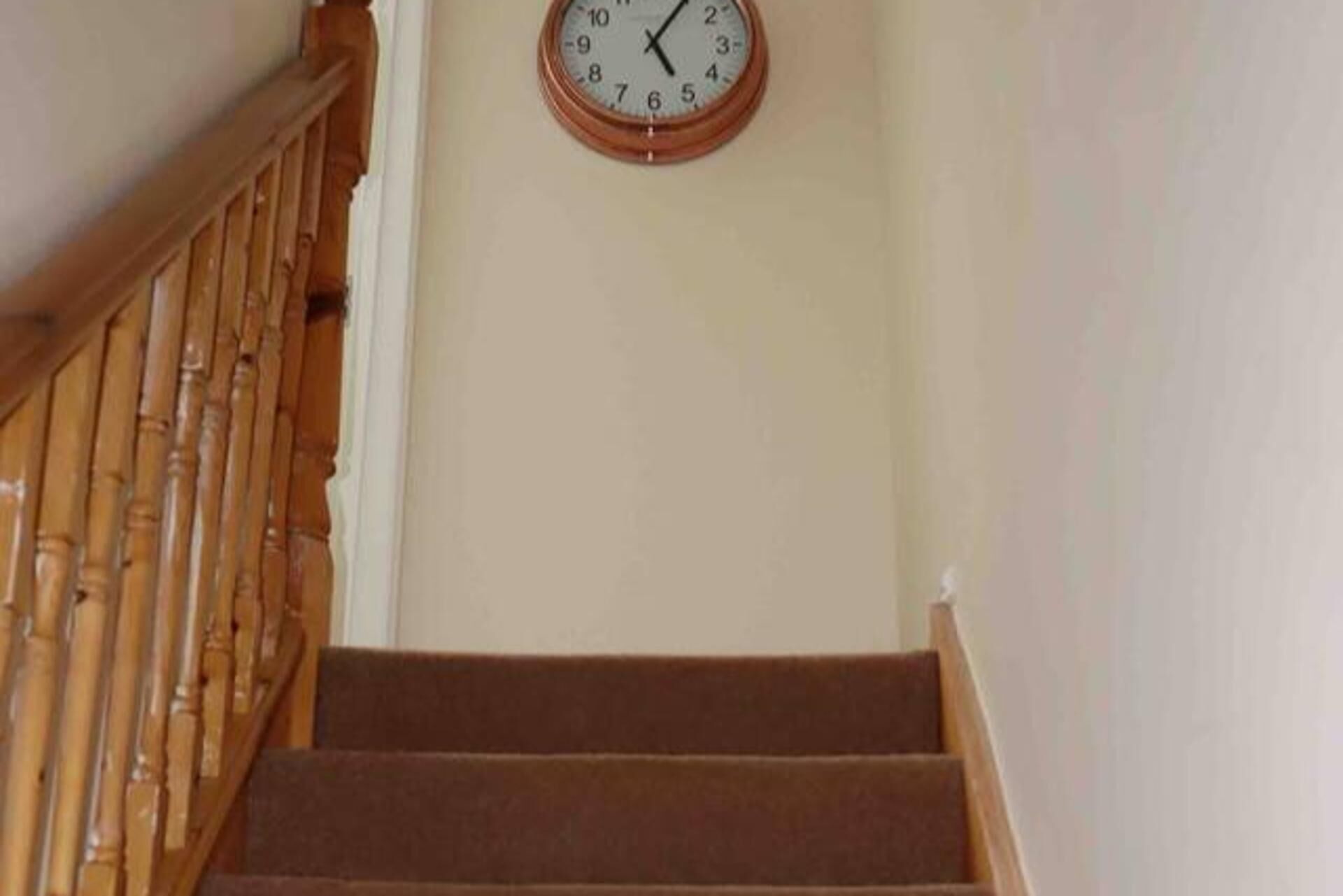 A staircase with a wooden handrail and a wall-mounted clock.