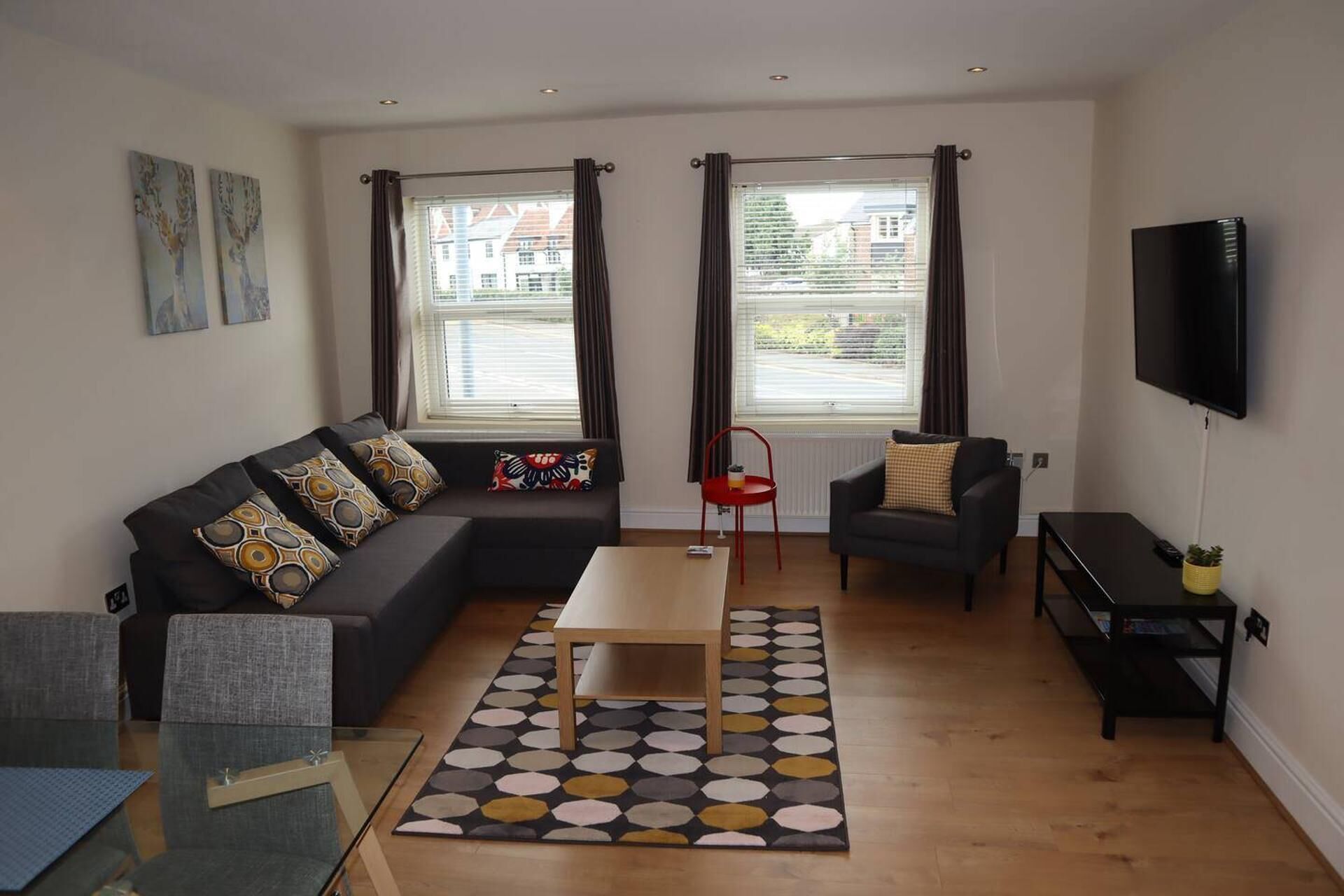 Een moderne woonkamer met een hoekbank, een klein bijzettafeltje en een aan de muur bevestigde televisie.
