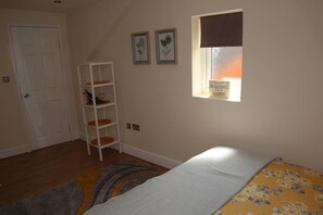 Un dormitorio con una cama, un ventanal con vistas, una puerta blanca y un estante blanco.
