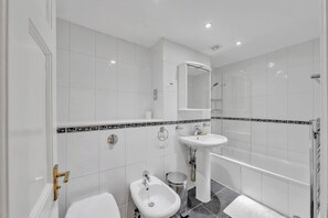 Ein modernes Badezimmer mit weißen Fliesen, einem Bidet, einem Waschbecken und einer Dusche.