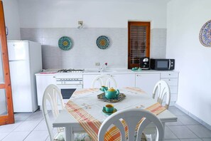 A compact kitchen with white cabinets, a stove, a microwave, and a sink. There are two decorative plates on the wall and a table with chairs set for dining. - Marina Guest House by Biddizzi Rari - near the beach and veranda with sea view (Sciacca)