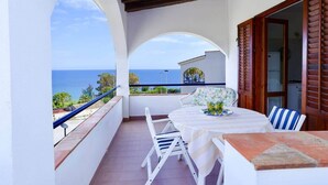 Un balcon avec une table et des chaises, une vue sur la mer et une porte en bois.