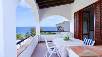 Un balcon avec une table et des chaises, une vue sur la mer et une porte en bois.