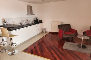 A modern kitchen with white cabinets, a black countertop, and a stainless steel sink. There are two bar stools and a red upholstered chair. - De Lux 4-Star Apartment with Ocean View, Rabac, Croatia (Rabac)